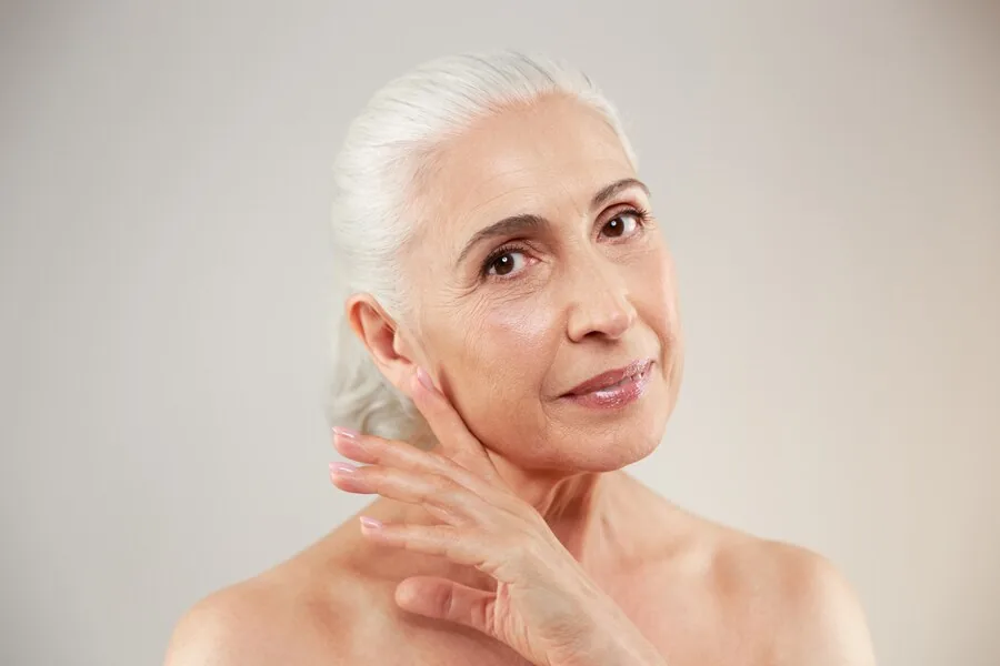 A silver-haired woman touching her cheek, her skin smooth and clear.