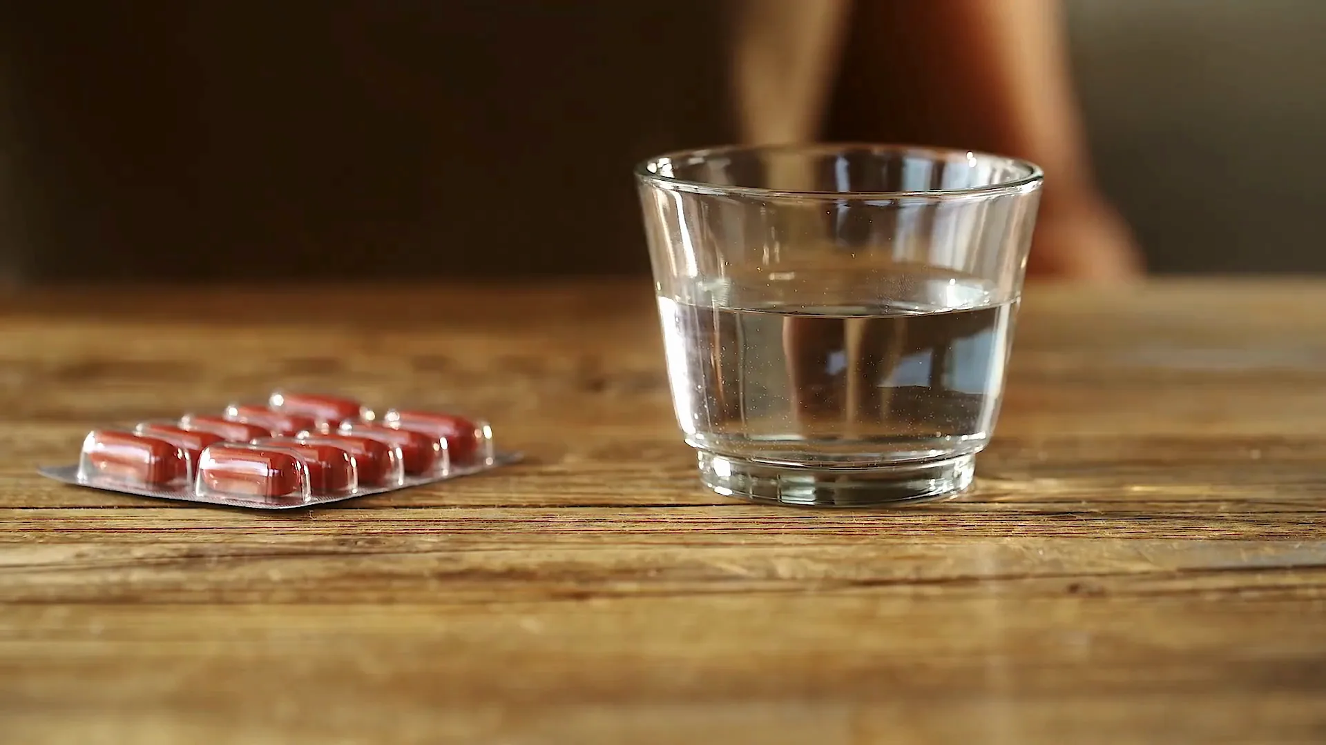 A blister pack of capsules beside a glass of water on a wooden table.