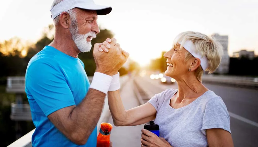 A senior couple in sportswear clasping hands after a run.