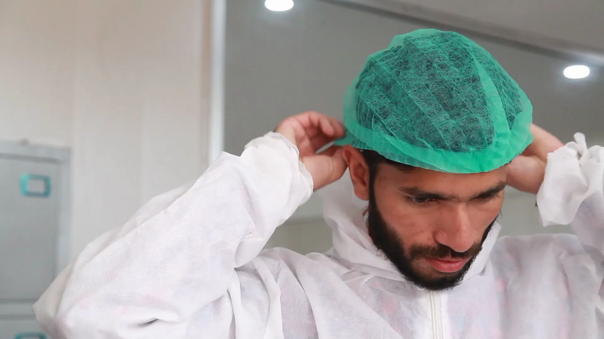 A production worker pulling on a hairnet over his cleanroom suit before entering the plant.