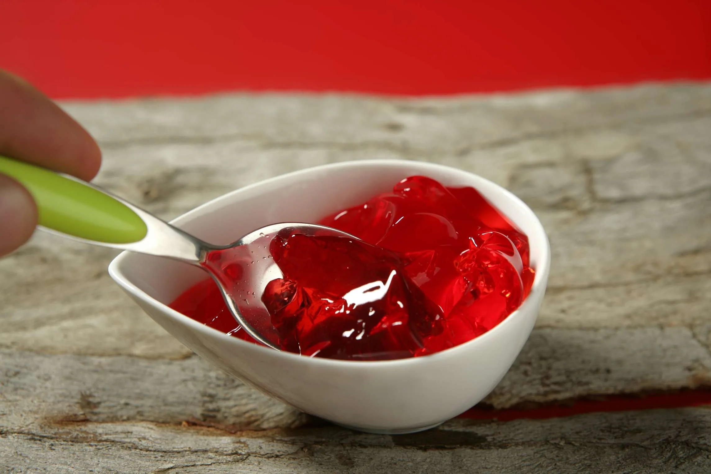A spoon lifting red jelly from a white bowl.