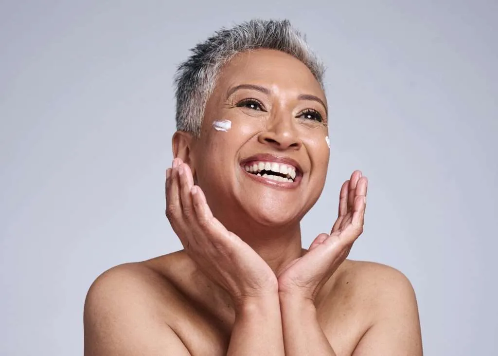 A smiling woman with a dab of moisturising cream on her cheek.