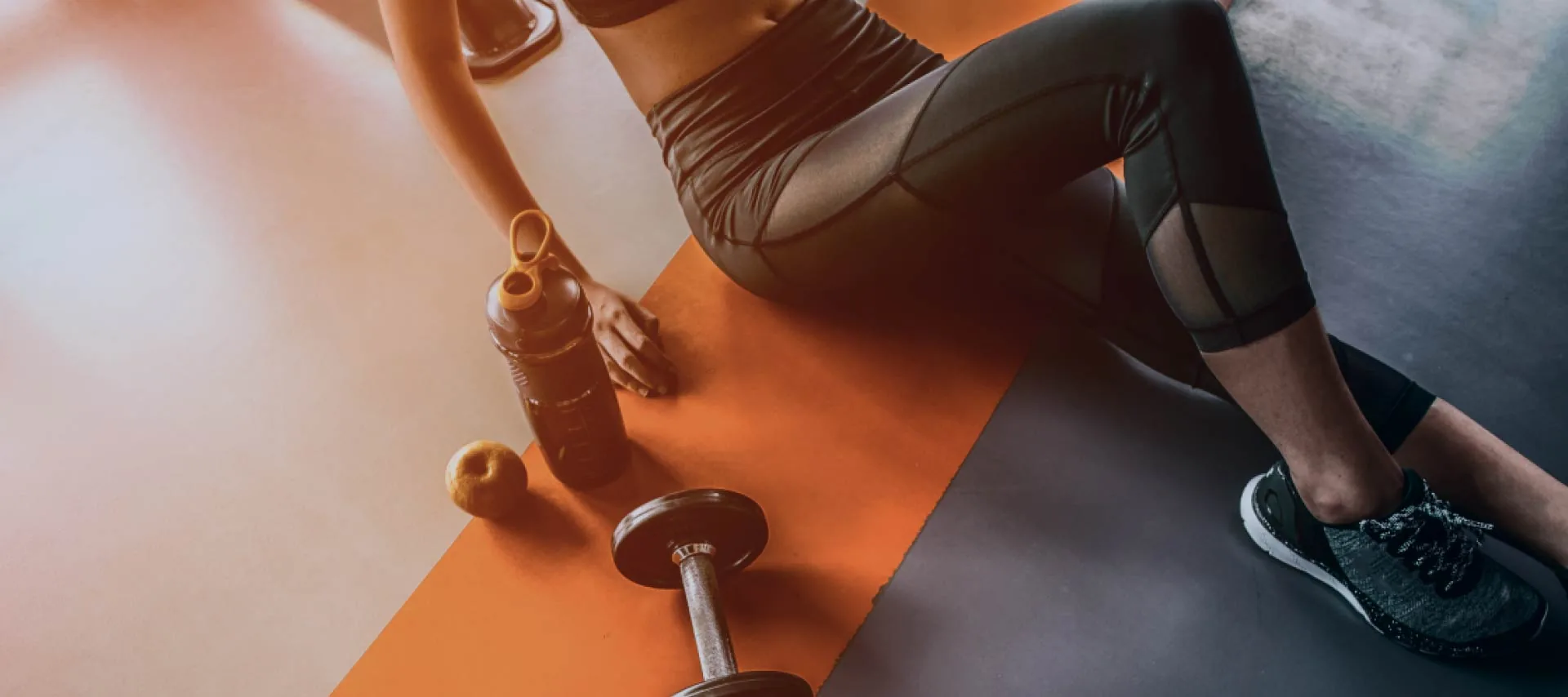 An athlete resting on a gym floor beside a dumbbell and a water bottle.