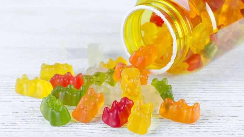 Colourful gummy bears spilling out of a glass jar.
