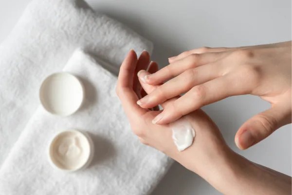 Hands smoothing moisturiser onto skin beside a folded white towel.