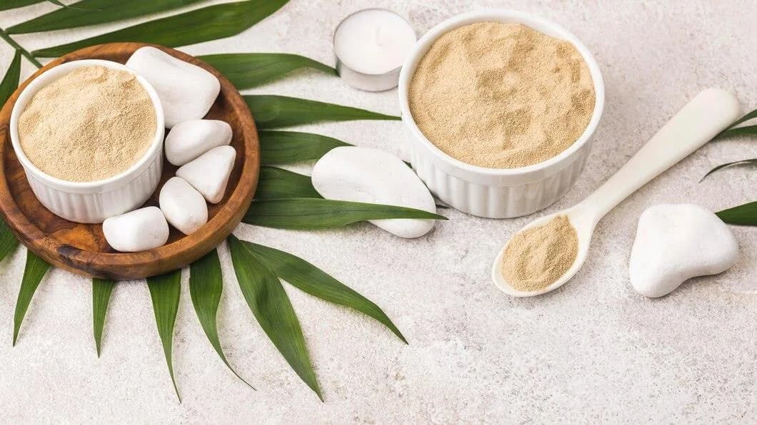 Bowls of fine collagen powder with white pebbles and palm leaves.