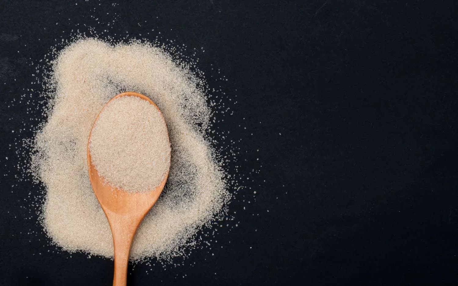 A wooden spoon of fine, pale gelatin powder on a dark background.