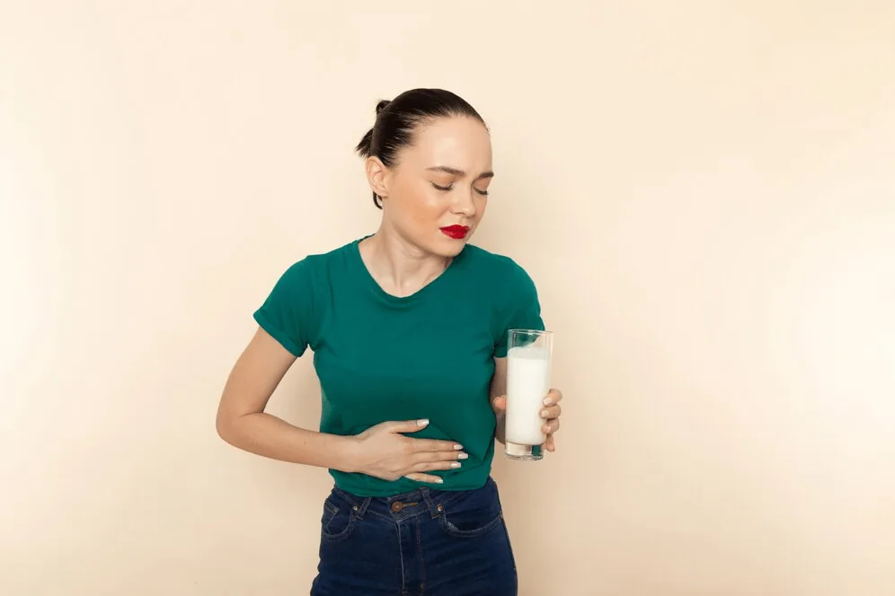 A woman holding her stomach with a glass of milk in her other hand.