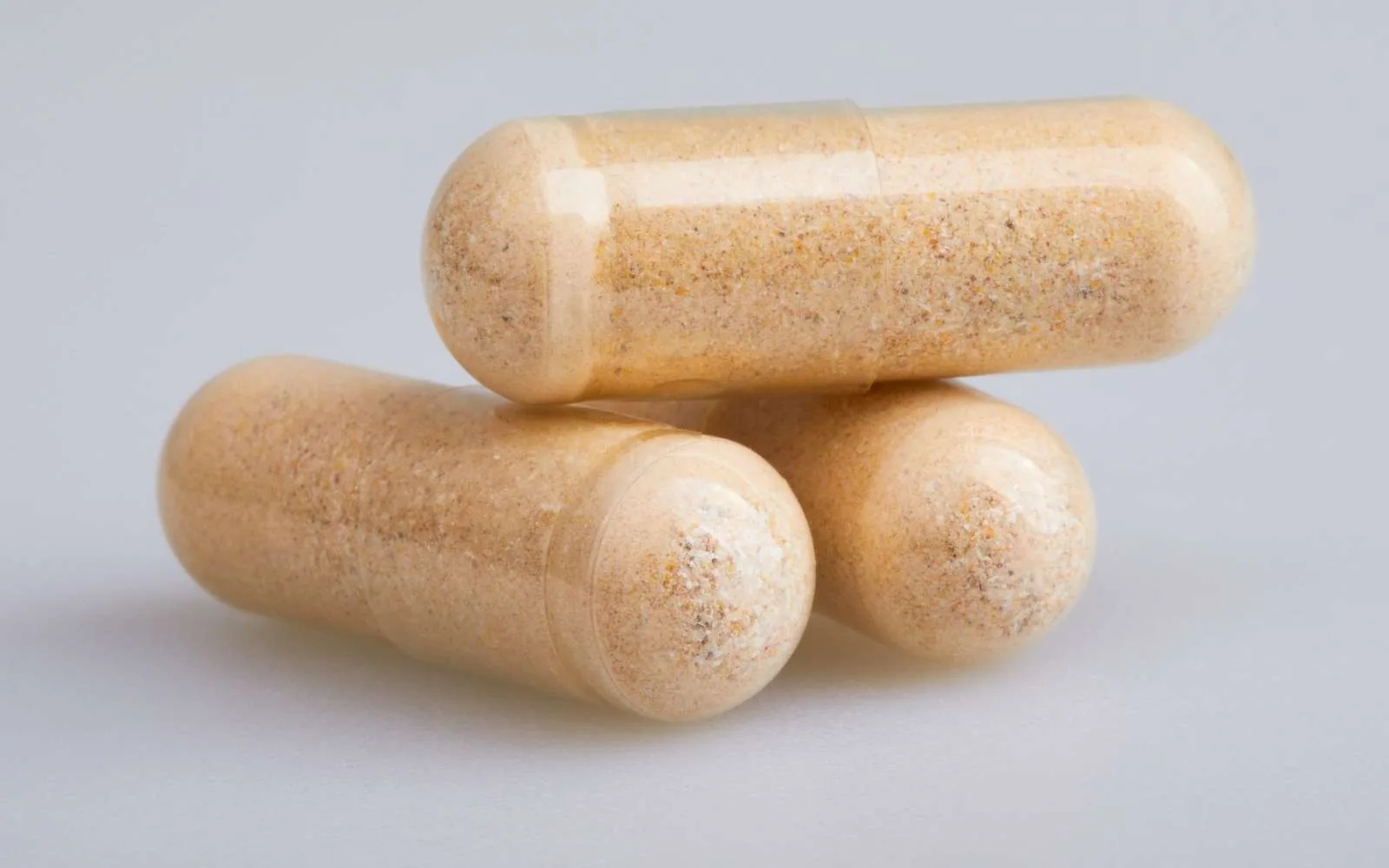 Two large beige hard capsules filled with powder, on grey.