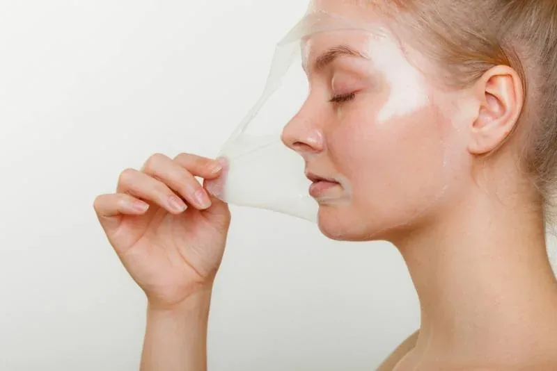 A woman peeling a clear gelatin mask from her face.
