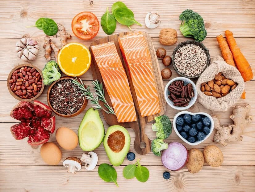 Salmon fillets, eggs, nuts, avocado and vegetables laid out on a wooden table.
