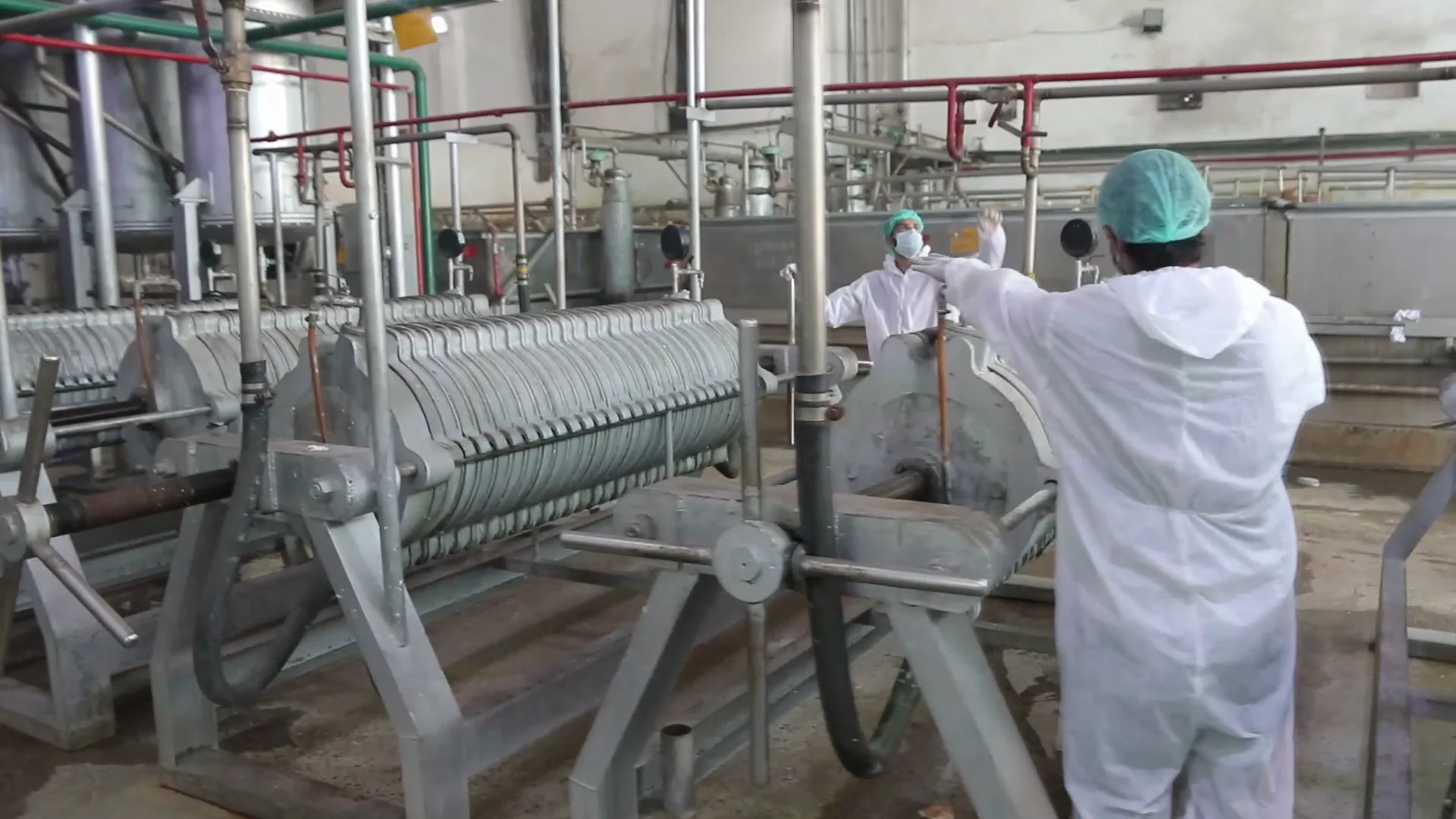 Two operators in cleanroom suits working along the gelatin filtration line.