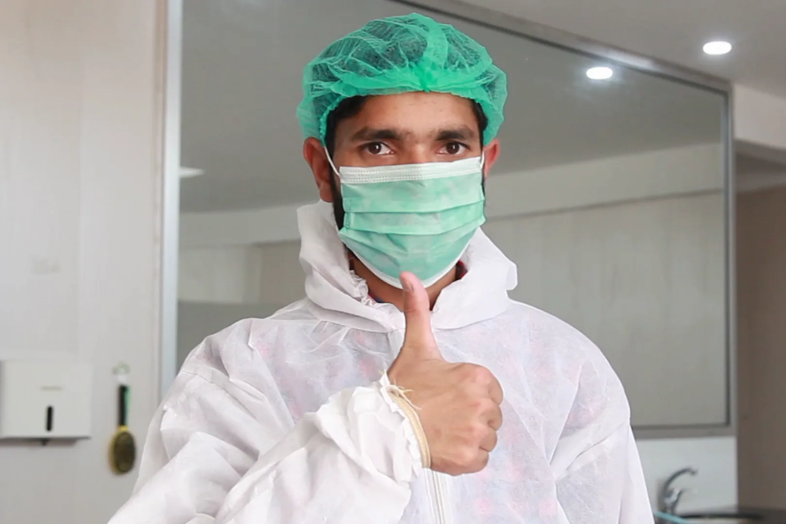 A Sadiq Gelatin worker in full hygiene kit — hairnet, mask and suit — giving a thumbs-up.