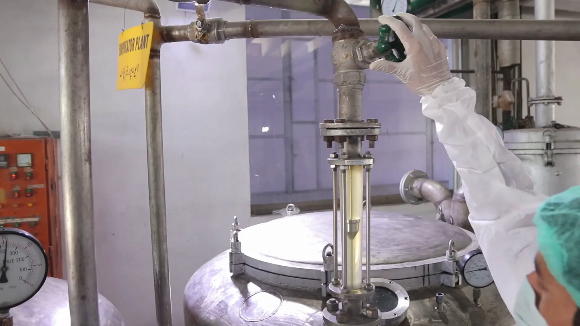 A gloved hand turning a valve above a reactor sight glass in the processing plant.