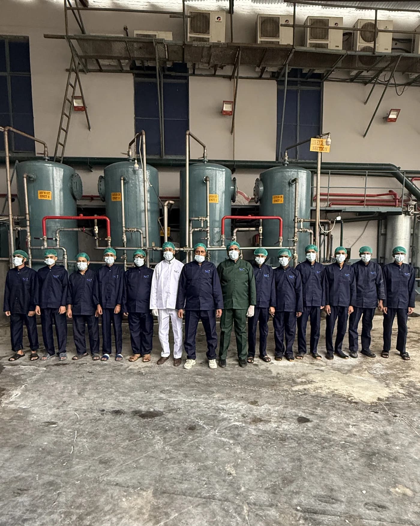 Sadiq Gelatin's plant team in uniform and hairnets beneath the four processing tanks.