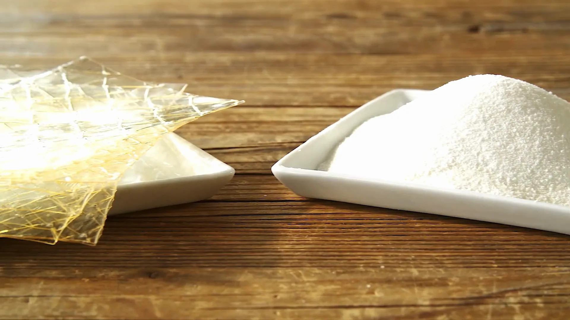 Clear gelatin sheets and a dish of gelatin powder on a wooden table.