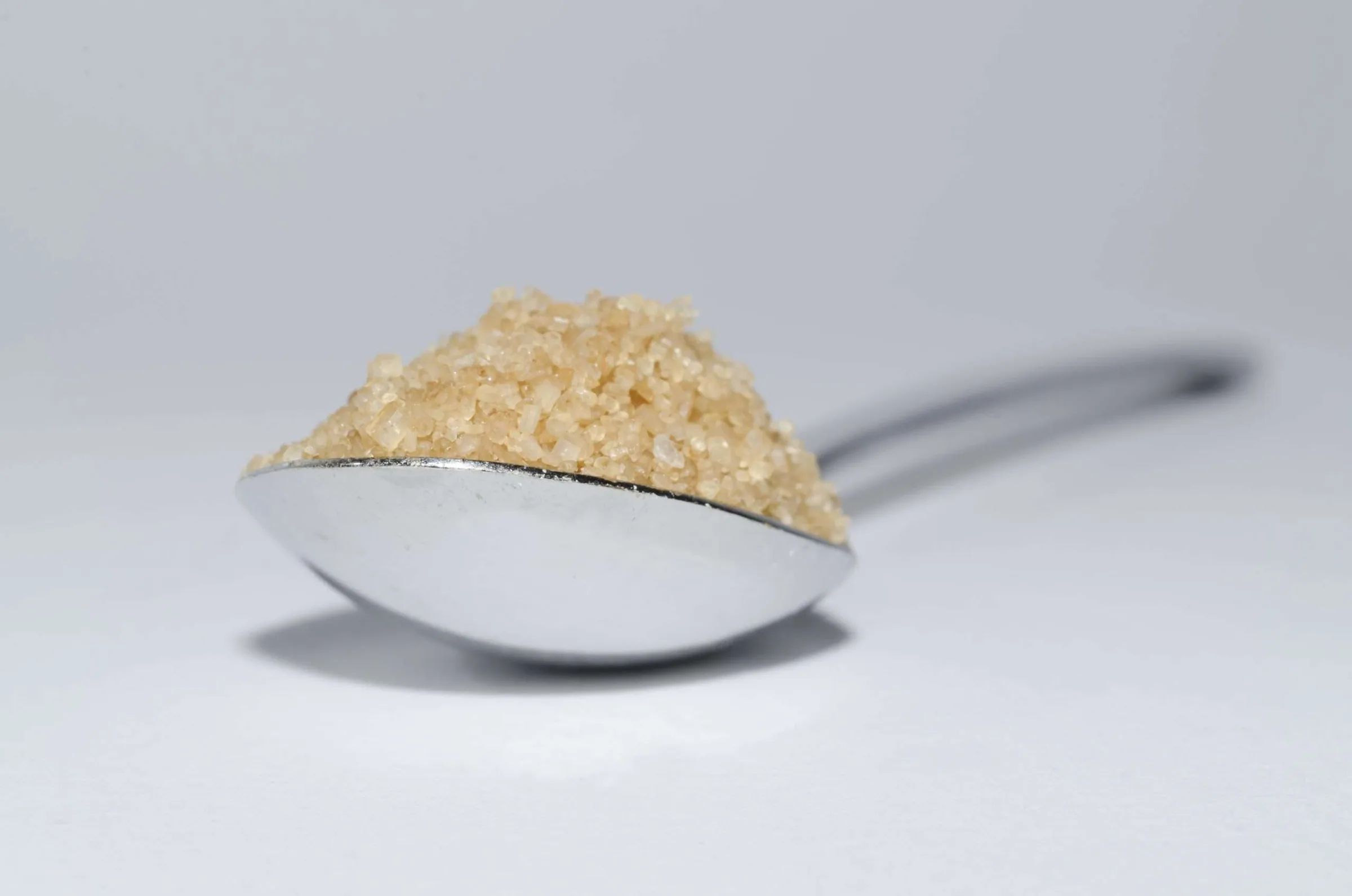 A metal spoon heaped with golden gelatin granules on a pale surface.